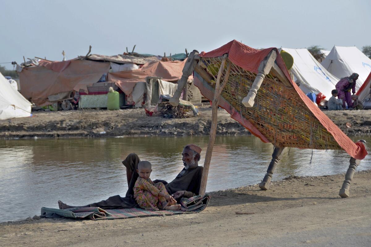 Flood victims sit under the shadow of a cot while they refuge on a roadside, in, Jaffarabad, a district of southwestern Baluchistan province, Pakistan, Monday, Sept. 19, 2022. Nearly three months after causing widespread destruction in Pakistan's crop-growing areas, flood waters are receding in the country, enabling some survivors to return home. The unprecedented deluges have wiped out the only income source for millions, with officials and experts saying the floods damaged 70% of the country's crops. (AP Photo/Zahid Hussain)