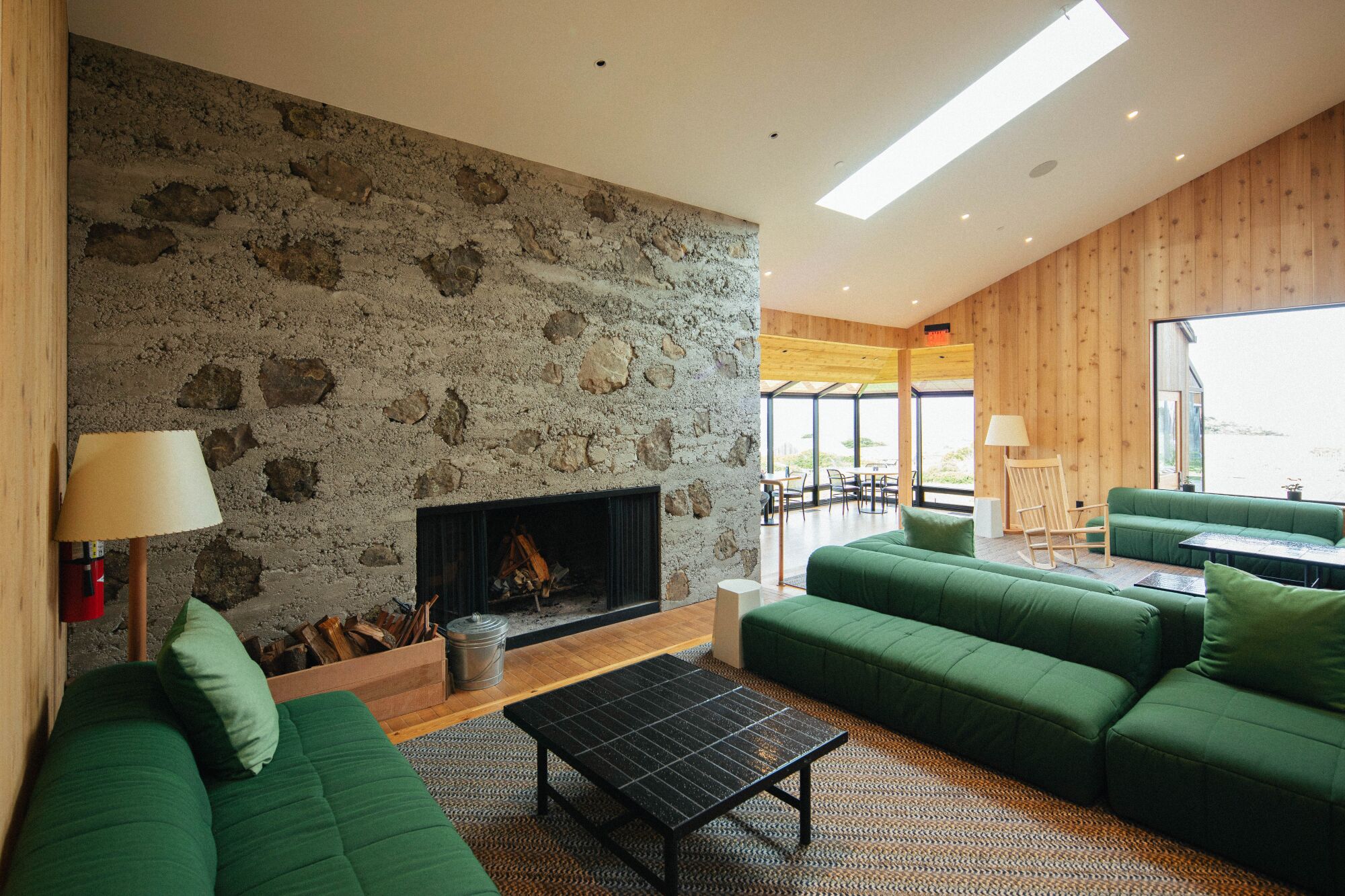 A room with wood walls, a large stone fireplace and green couches.