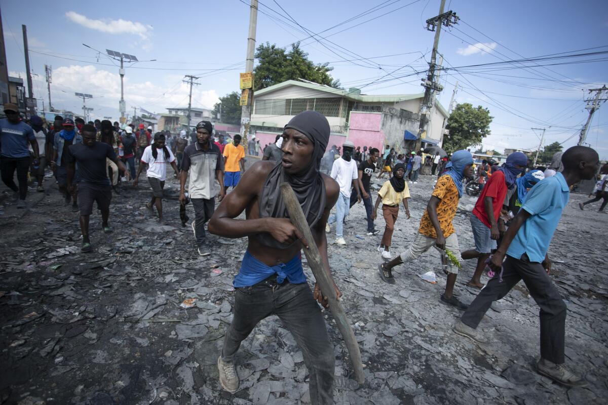 Protesters, one carrying a piece of wood carved like a gun, march in Haiti.