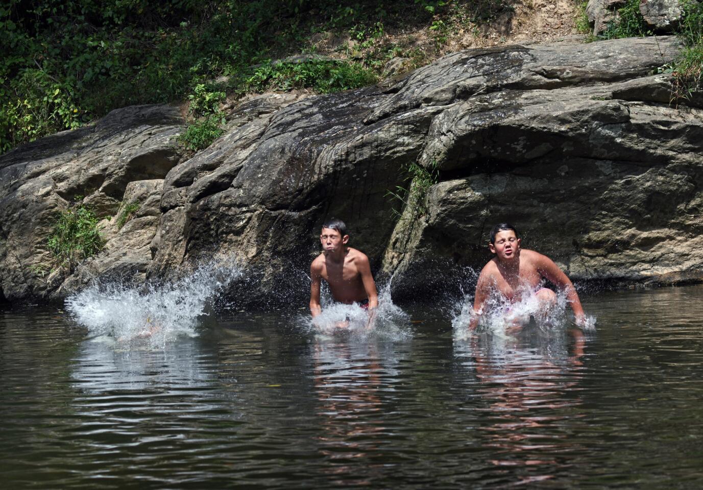 Forest Hill, Md.--August 19, 2019-- The Holmes brothers of Aberdeen, from left, Canon, 8, Kaleb, 12 and Mason, 10, jump off a rock into Deer Creek to cool off from the over 90 degree hot weather at Rocks State Park.