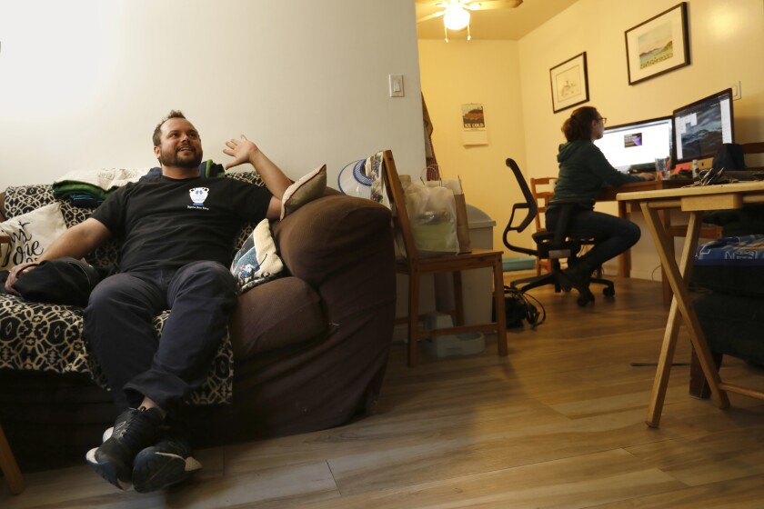 Jack Shain sits on a couch while Cara Ferraro works at her computer in the background