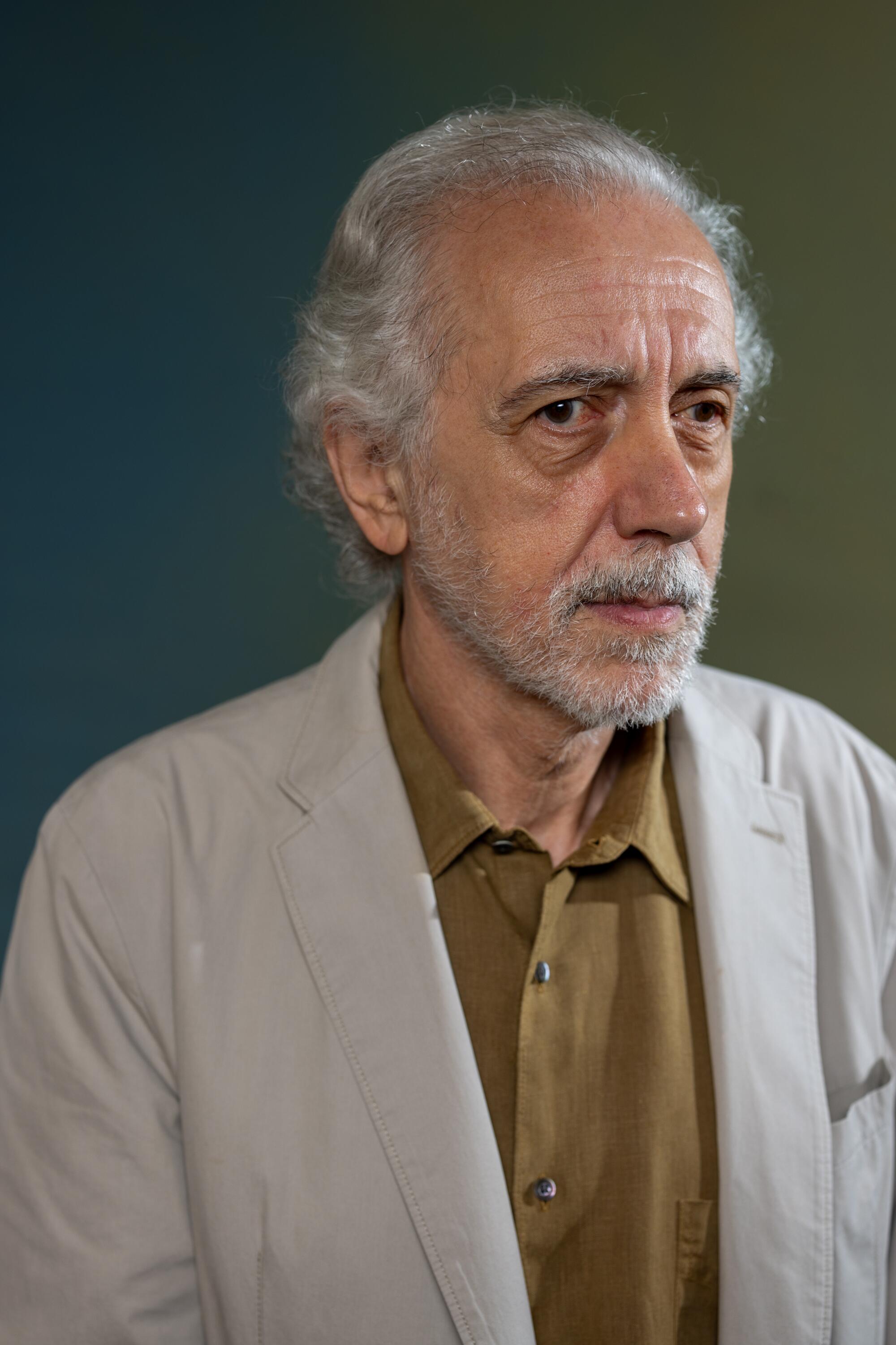 Fernando Trueba looks to the side while wearing a brown shirt and white jacket.