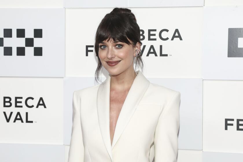 A woman with brown hair and bangs wears a white suit. She poses for pictures at a red carpet event. 