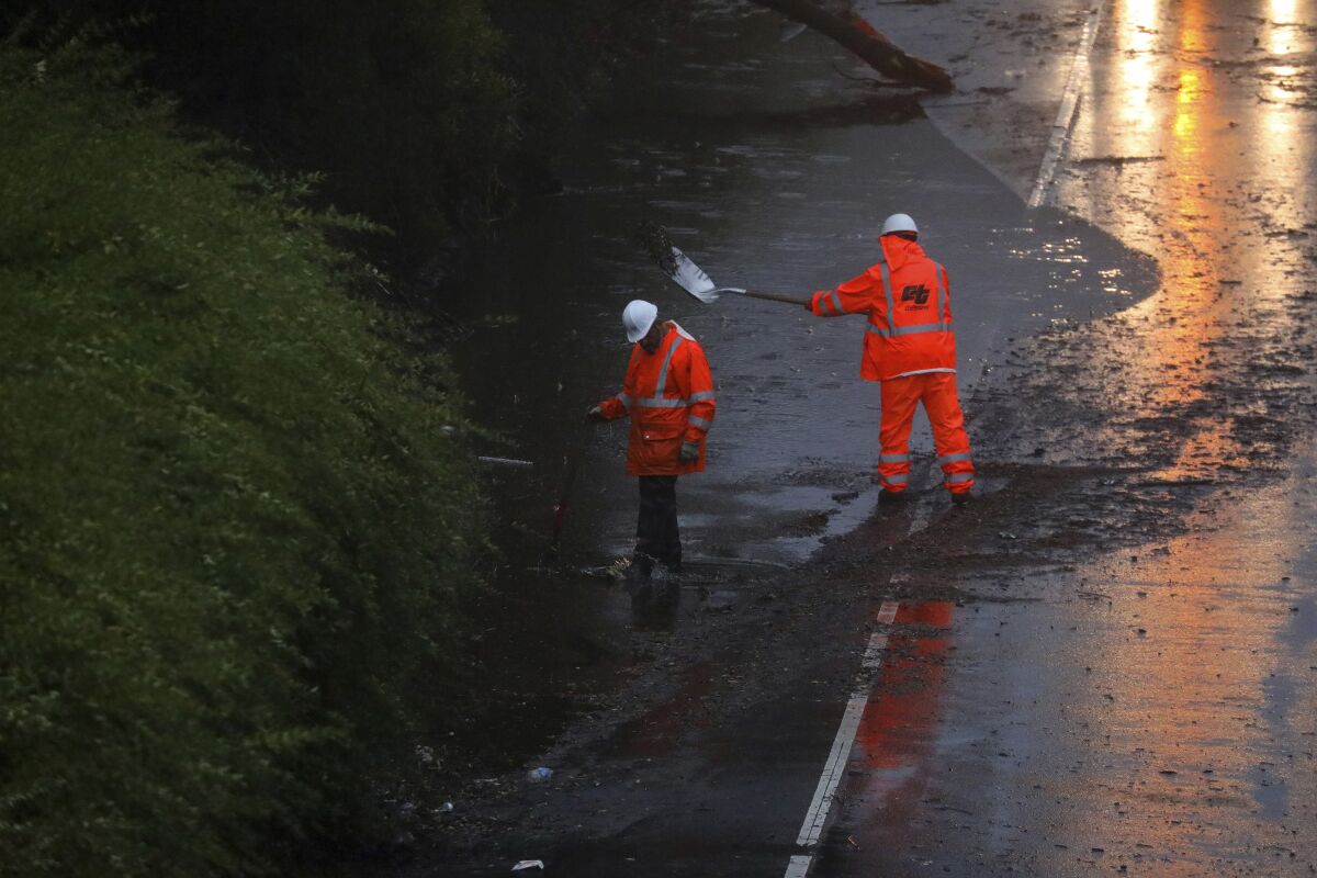 Two people in orange clothes shovel something on the side of a flooded road.