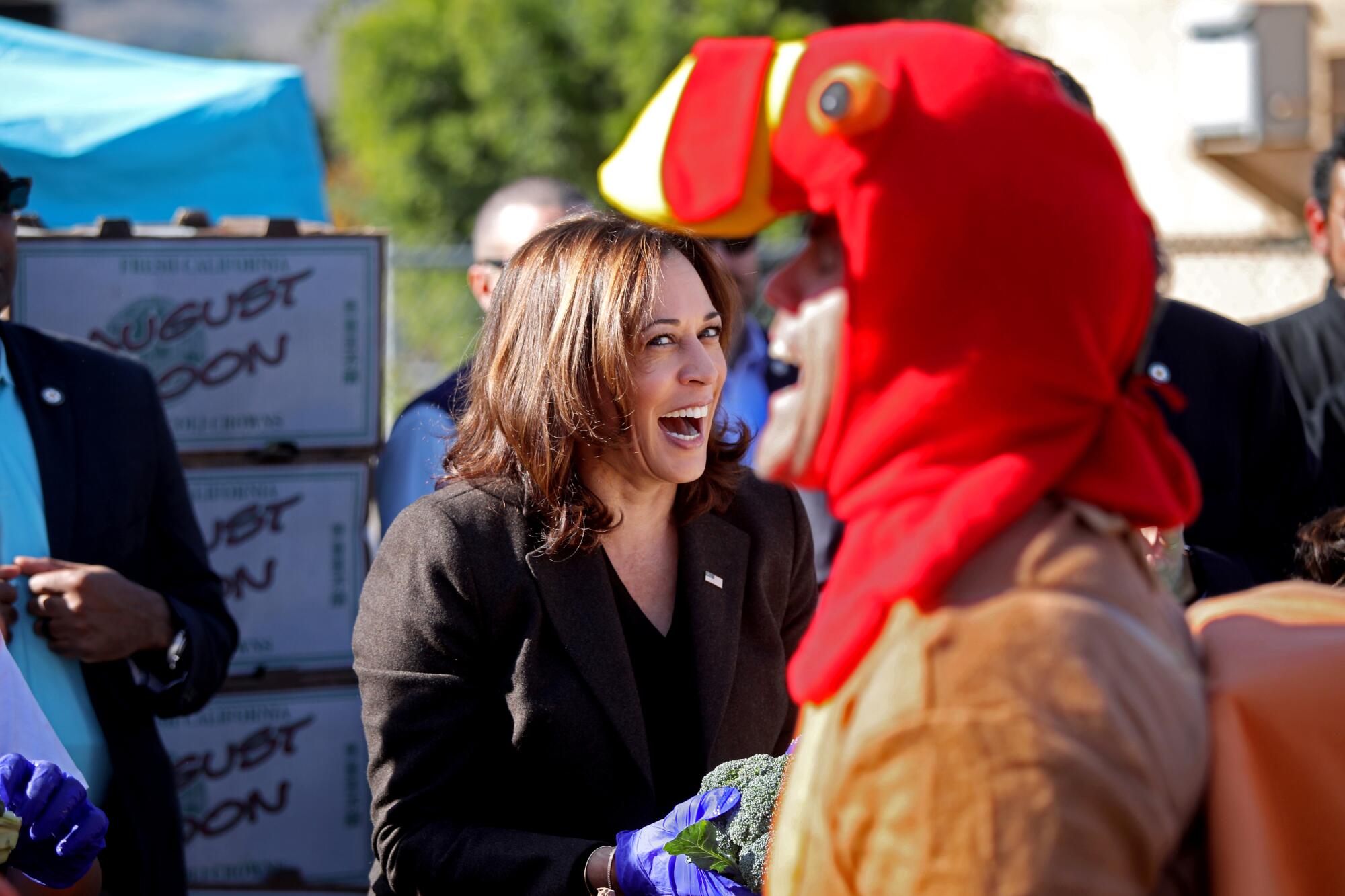 A smiling woman looks at a person dressed as a turkey.