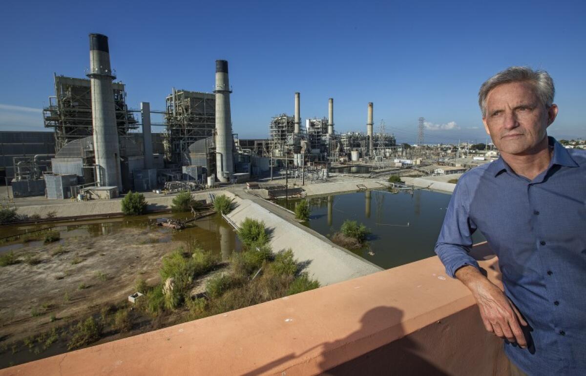 A man in a button-down shirt leans an elbow on a railing. In the background is a power plant.