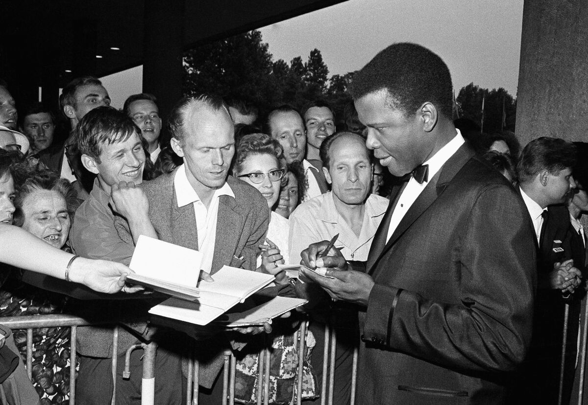 FILE - Sidney Poitier signs autographs before the opening of the 14th International Film Festival at the West Berlin congress hall on June 26, 1964 in Berlin. Poitier, the groundbreaking actor and enduring inspiration who transformed how Black people were portrayed on screen, became the first Black actor to win an Academy Award for best lead performance and the first to be a top box-office draw, died Thursday, Jan. 6, 2022 in the Bahamas. He was 94. (AP Photo/Edwin Reichert, File)
