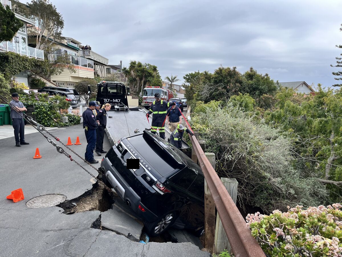 An SUV wedged in a sinkhole under a guard rail on the side of a street