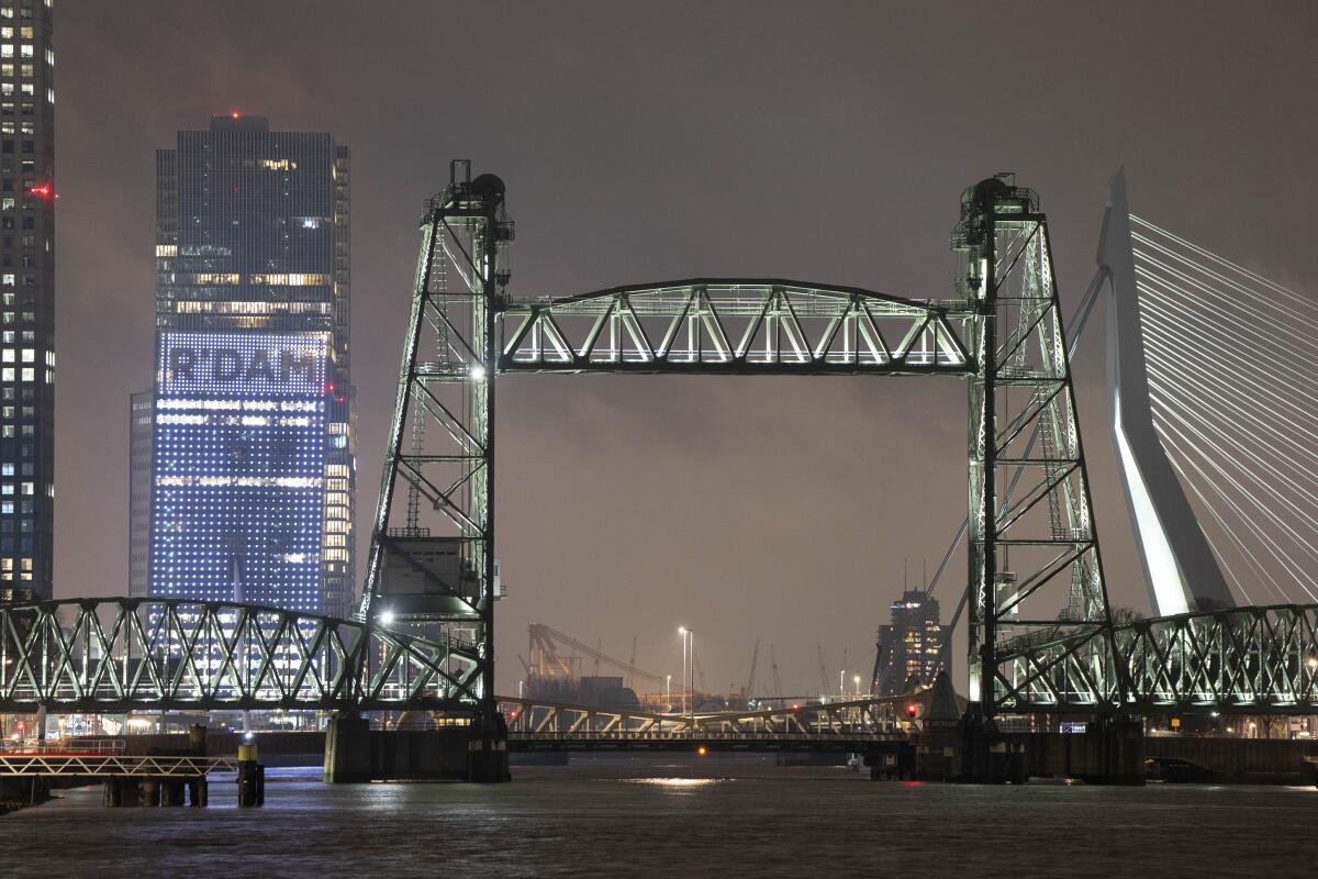 A view of a bridge with a building in the background with an illuminated sign that says, "R'Dam"