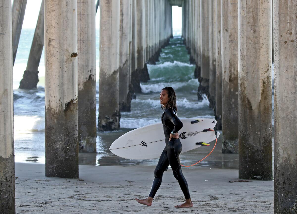 Kevin Tran walks under the pier after a day of surfing in Huntington Beach on July 31.