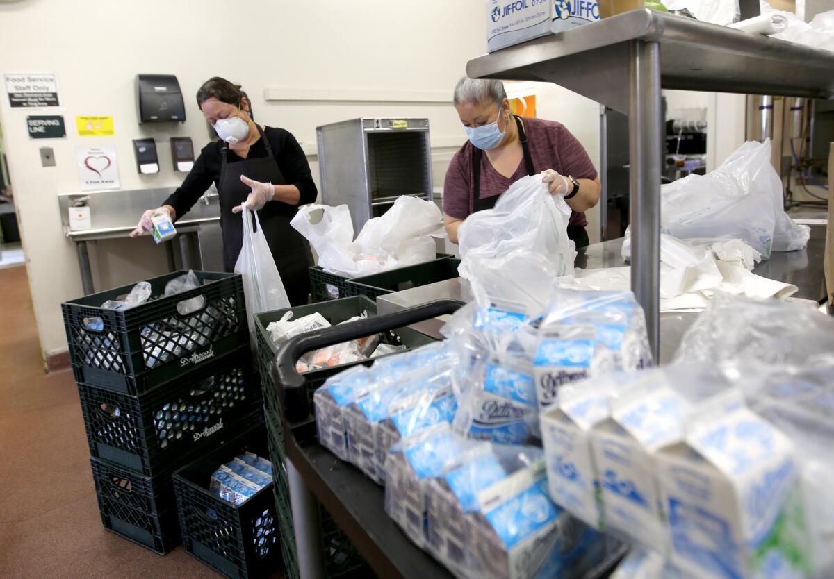 Burbank Unified cafeteria workers Carmen Cezena, left, and Norma de la Torre prepare milk and juice bags for the five-day meal packages for students across the district at Burbank Middle School on Tuesday.