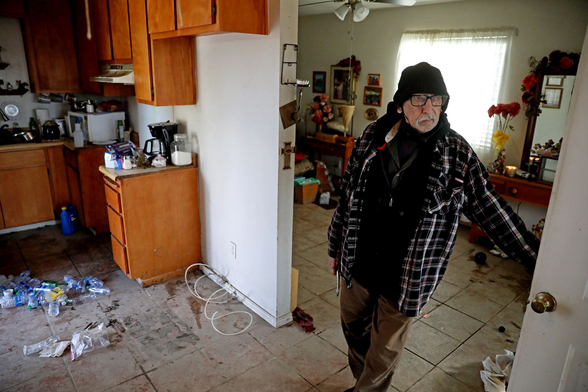 A man stands inside a small kitchen with damaged flooring.