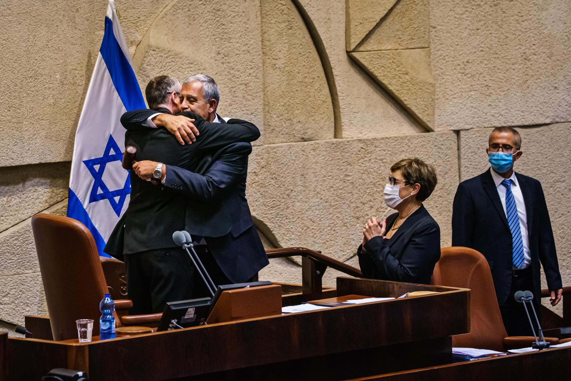 Israeli politicians hug at desk.