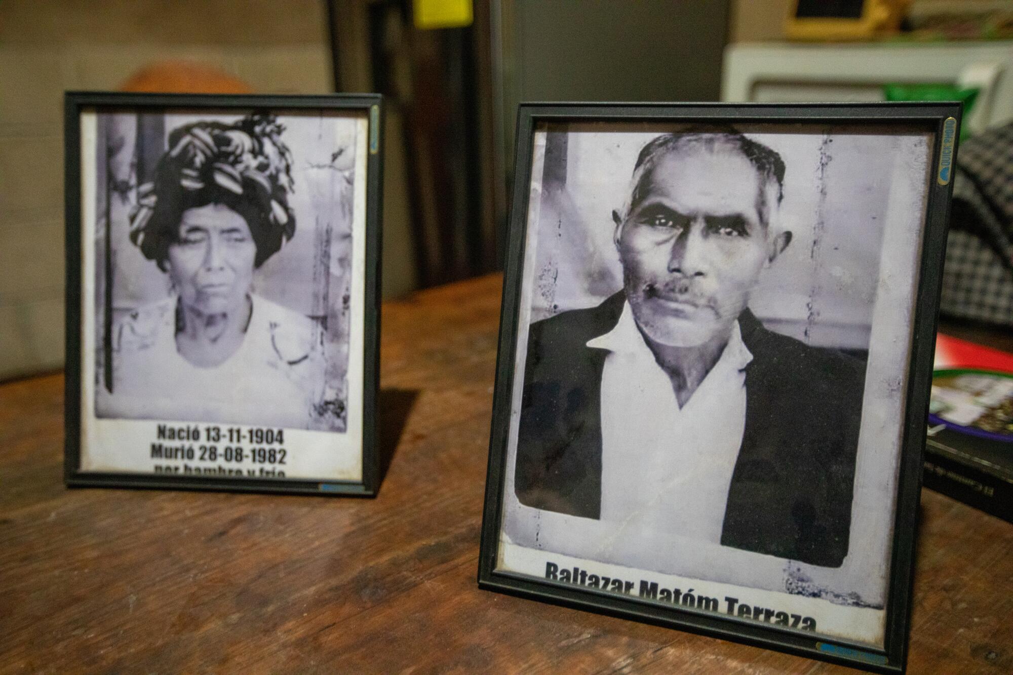Two framed black-and-white portraits of a Maya woman, left, and an older man sit on a table. 
