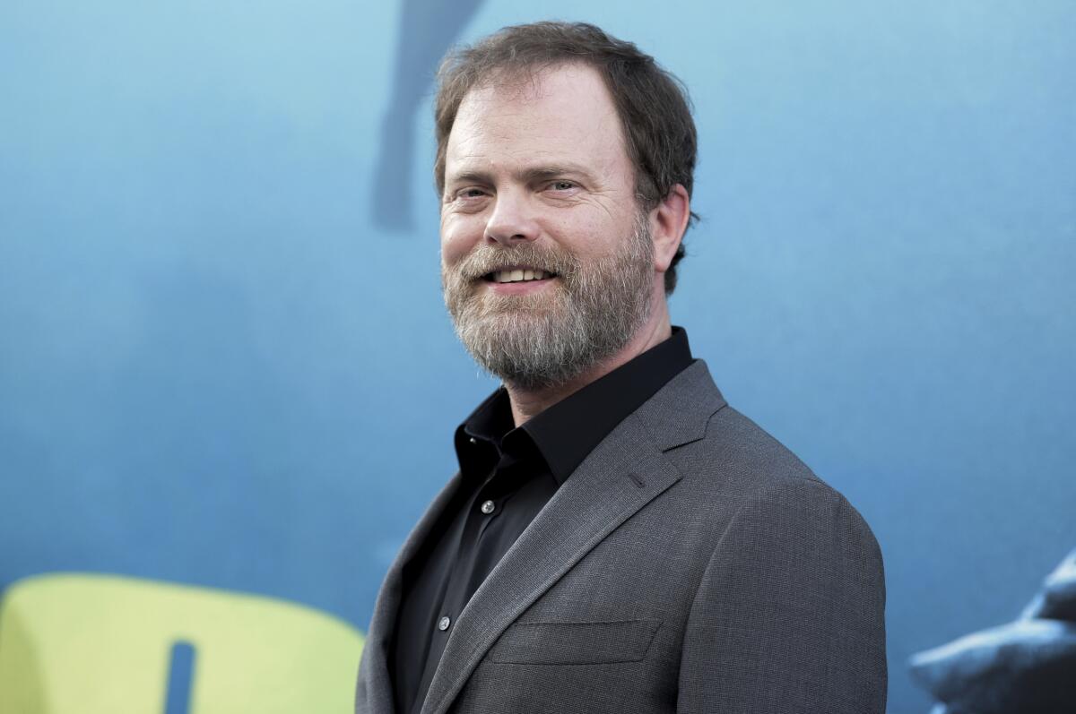 A bearded man in a sport coat and dark shirt poses upon arrival at an event