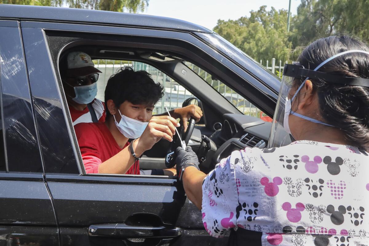 Jorge Angel Llamas, left, takes a COVID-19 test under the supervision of nurse Karen Barringer in Chula Vista on Friday.