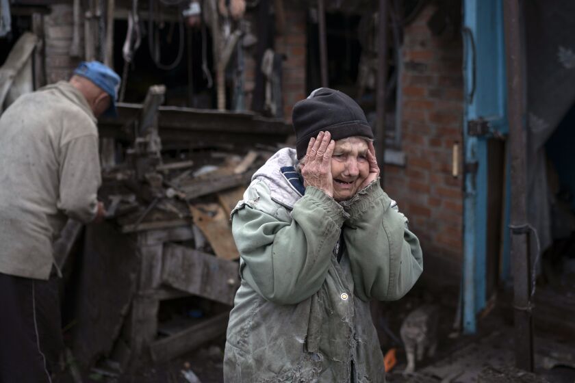 Valentina Bondarenko reacts as she stands with her husband Leonid outside their house that was heavily damaged after a Russian attack in Sloviansk, Ukraine, Tuesday, Sept. 27, 2022. The 78-year-old woman was at garden and fell on the ground at the moment of the explosion. "Everything flew and I started to run away", says Valentina. (AP Photo/Leo Correa)