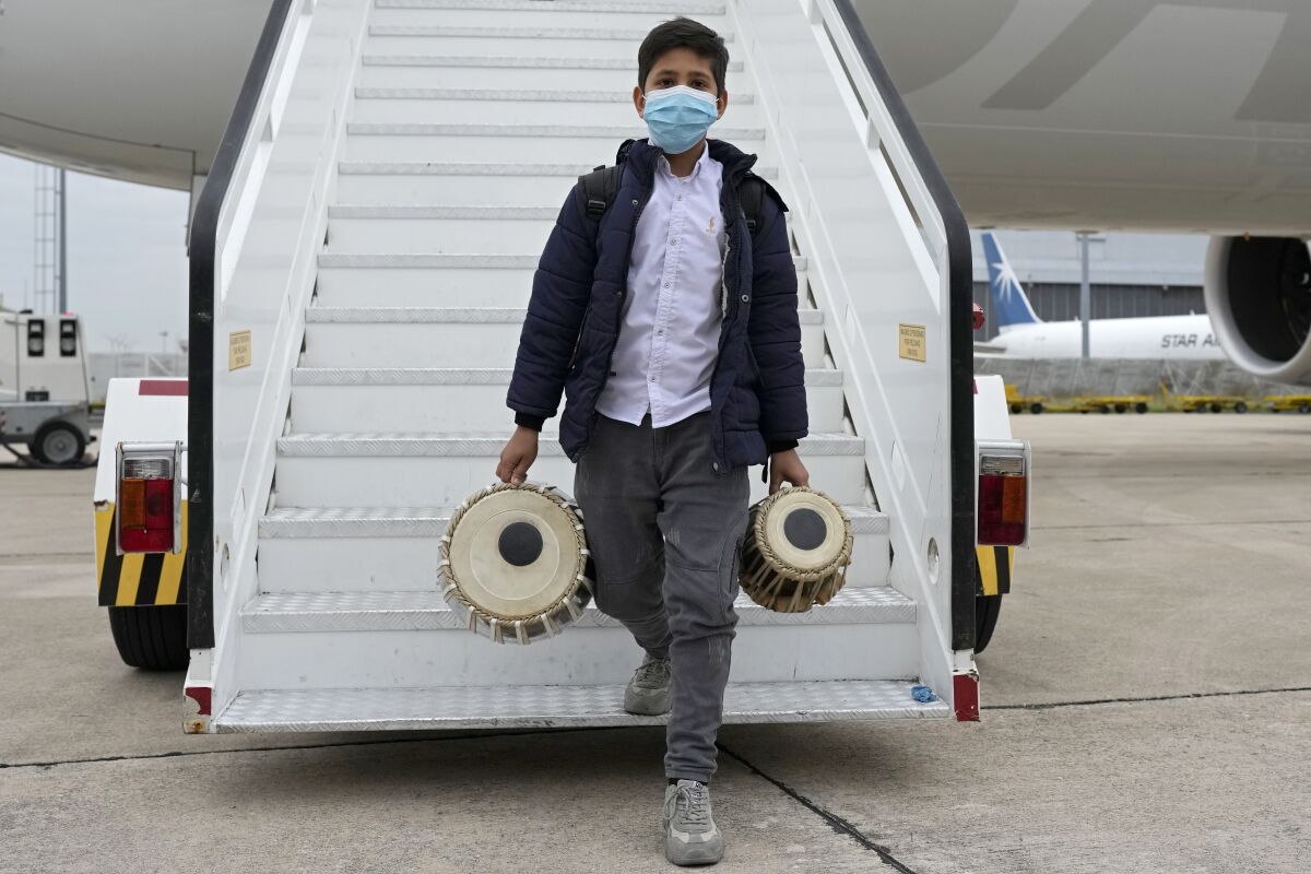 An Afghan boy carrying musical instruments disembarks from an airplane at Lisbon military airport, Monday, Dec. 13, 2021. A group of 273 students, faculty members and their families from the Afghanistan National Institute of Music arrived Monday in Portugal, where they are being granted asylum and where they hope to rebuild their acclaimed school.(AP Photo/Armando Franca)