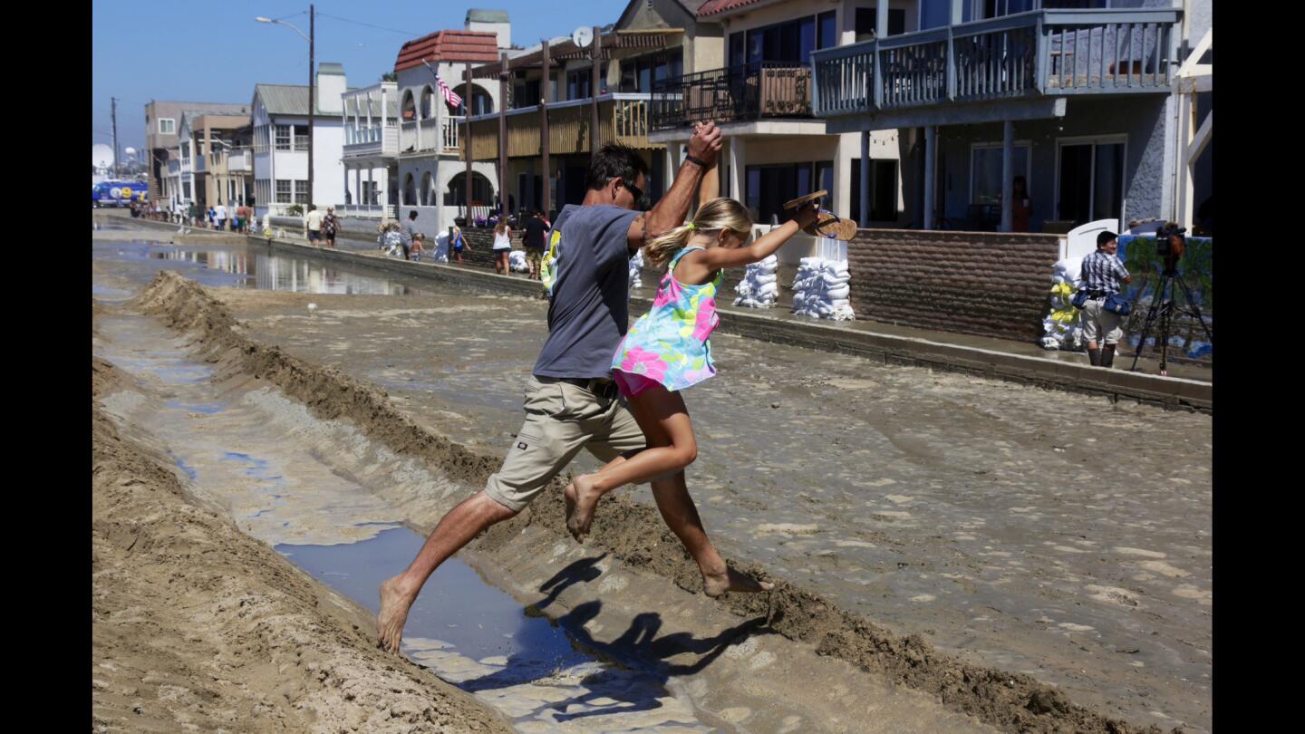 Steve Trachta and his 8-year-old daughter, Alex, leap over a ditch created to channel water during high surf away from homes along Seal Beach.