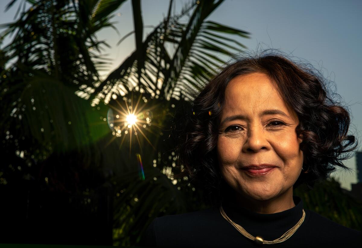 A smiling woman  next to palm fronds. 