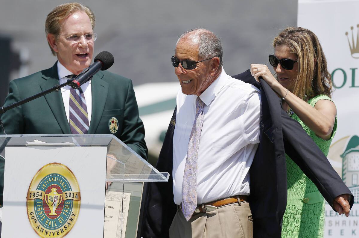FILE - Monica Seles, right, helps Nick Bollettieri with a blazer as Hall of Fame chairman of the board Christopher Clouser, left, looks on during Bollettieri's induction into the International Tennis Hall of Fame in Newport, R.I., Saturday, July 12, 2014. Nick Bollettieri, the Hall of Fame tennis coach who worked with some of the sport’s biggest stars and founded an academy that revolutionized the development of young athletes, has died. He was 91. Bollettieri passed away Sunday night, Dec. 4, 2022, at home in Florida after a series of health issues, his manager, Steve Shulla, said in a telephone interview with The Associated Press on Monday. (AP Photo/Michael Dwyer, File)