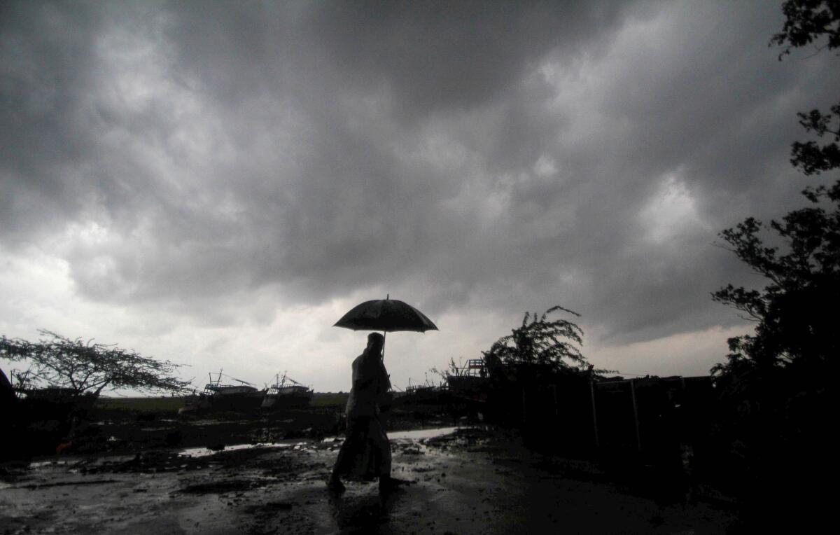 A villager holds an umbrella as dark clouds loom over Balasore district in Odisha, India, Tuesday, May 25, 2021.