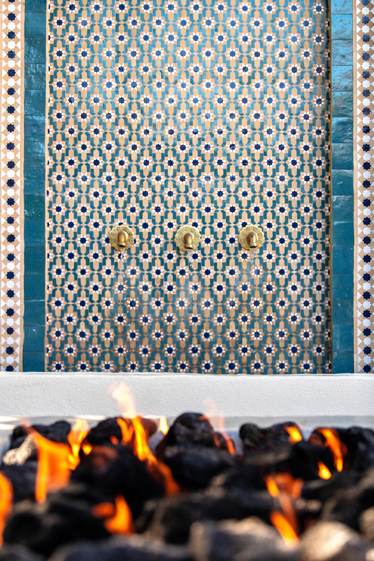 Behind a fire pit is a water feature lined in Moroccan tile bearing a floral pattern.