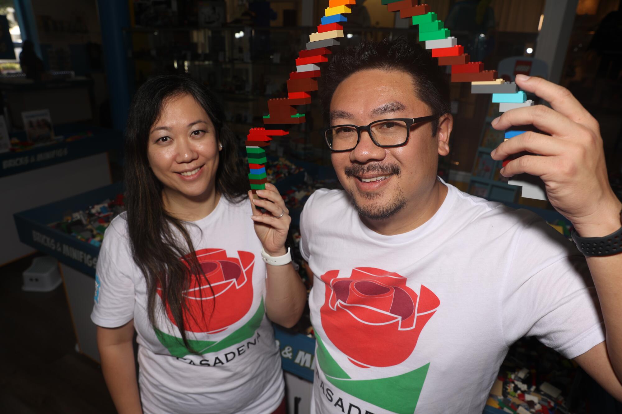 Betty Poquez, left, Rob Poquez hold an arch of Lego bricks while wearing shirts with a rose design and the name "Pasadena"