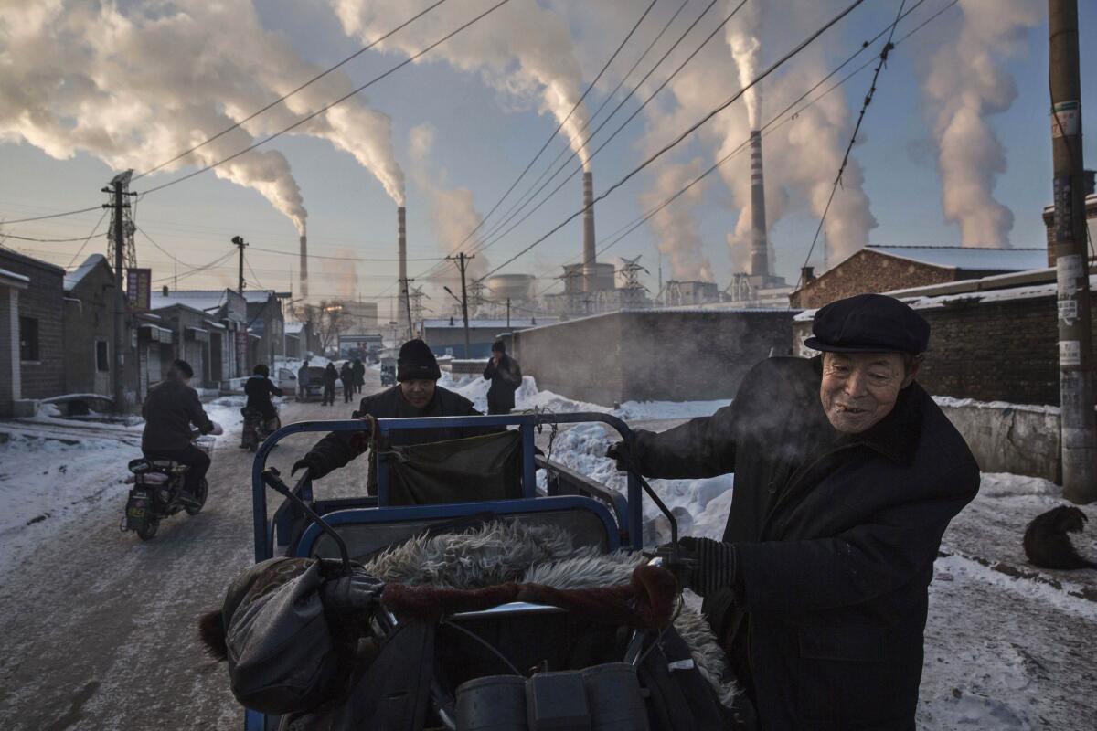 Smoke billows from stacks as men pull a tricycle in a neighborhood next to a coal-fired power plant in Shanxi, China.