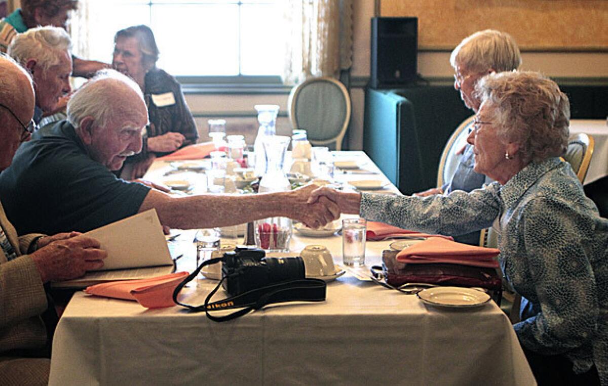 Classmates George Azadian and Leona Doolittle Wesley shake hands across the table during a luncheon for 29 members of the Manual Arts Class of 1941.