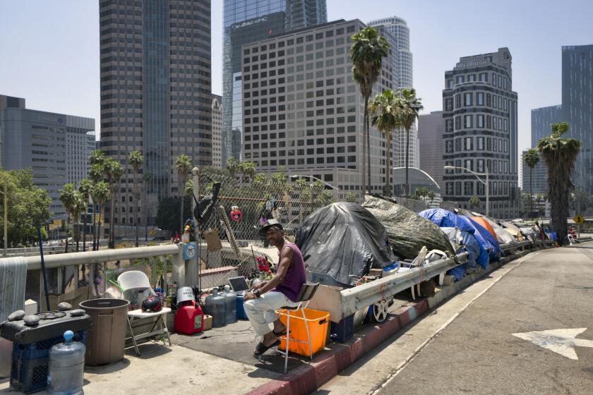 FILE - A homeless man sits at his street side tent along the Interstate 110 freeway along downtown Los Angeles' skyline, on Thursday, May 10, 2018. A federal judge has approved a settlement of a lawsuit against Los Angeles over efforts to deal with a homelessness crisis. Under the deal signed Thursday, Sept. 28, 2023 Los Angeles County and city will spend billions of dollars to provide more housing and support services for the unhoused. (AP Photo/Richard Vogel,File)