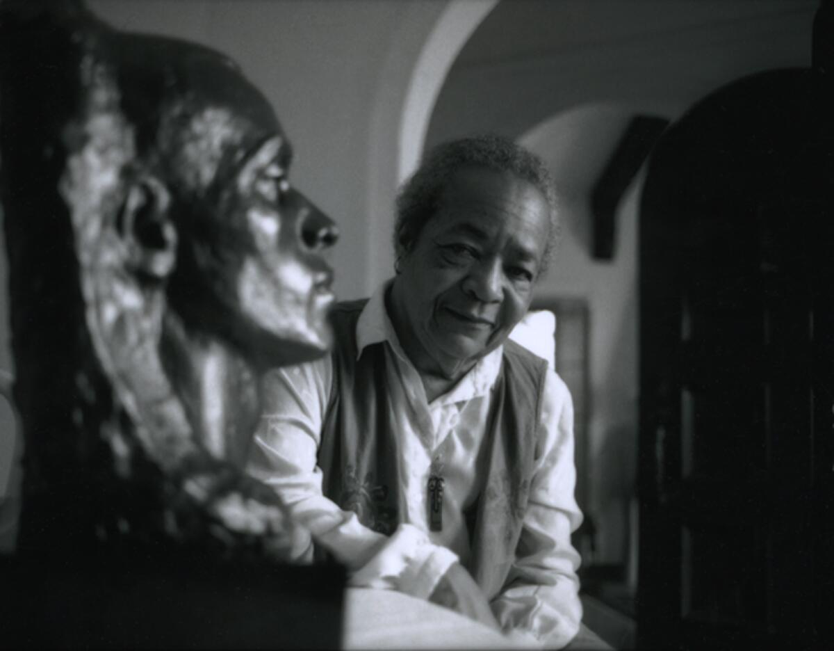 A woman sits next to a bronze bust.