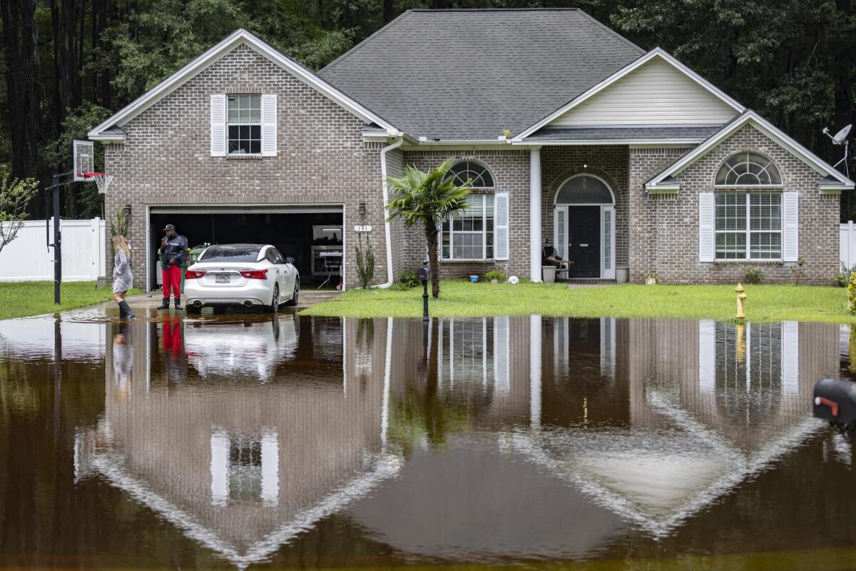 A man and woman stand just oustide their garage as floodwater surrounds their home. 