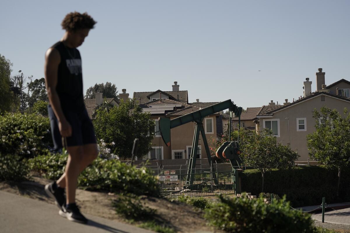 A man walks along the street as a pump jack extracts oil at a drilling site next to homes in Signal Hill, California. 