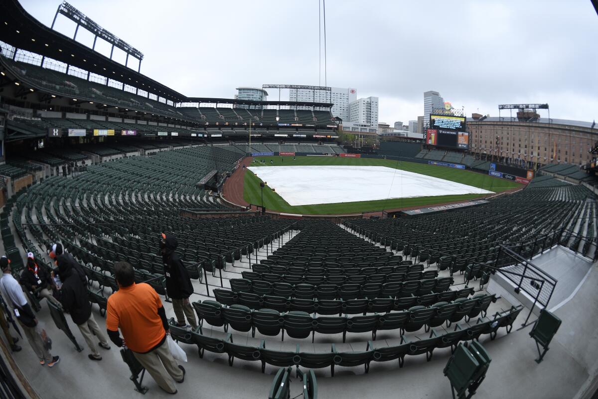 In this picture taken with a fisheye lens, the tarp lays on the field and the scoreboard signals the postponement of a baseball game between the Baltimore Orioles and the Seattle Mariners due to inclement weather, Wednesday, April 14, 2021, in Baltimore. The game will be played as a doubleheader tomorrow. (AP Photo/Nick Wass)