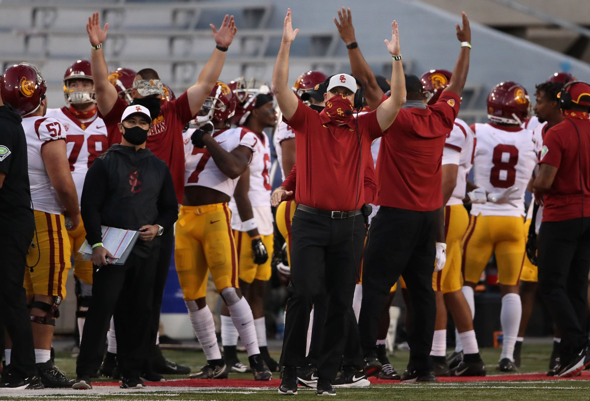 USC coach Clay Helton reacts after a touchdown by raising his arms while on the sideline. Players and staff are behind him.