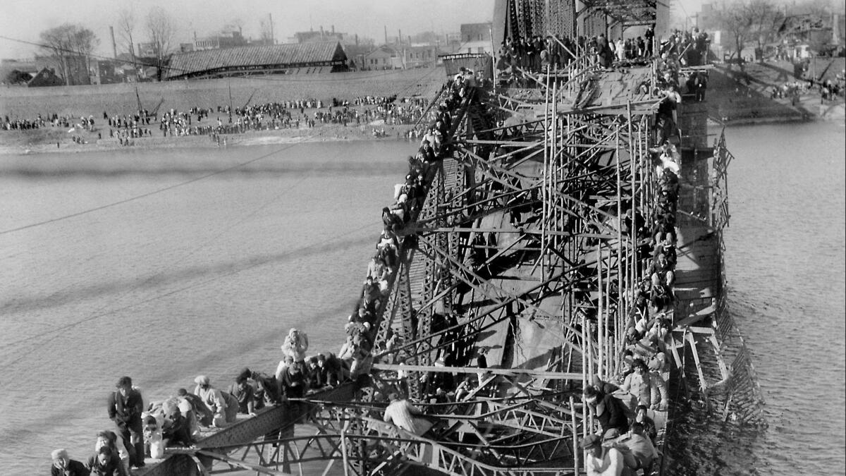 Max Desfor's Dec. 4, 1950 photo shows people near Pyongyang, North Korea, crawling over a bridge's twisted girders as they flee south across the Taedong River to escape Chinese troops.