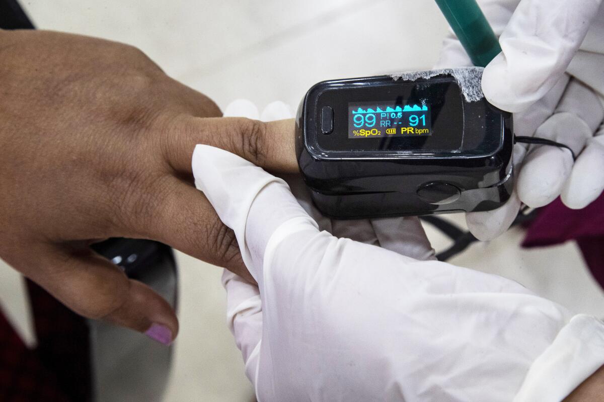 Two gloved hands put a measuring device on a finger of another person.