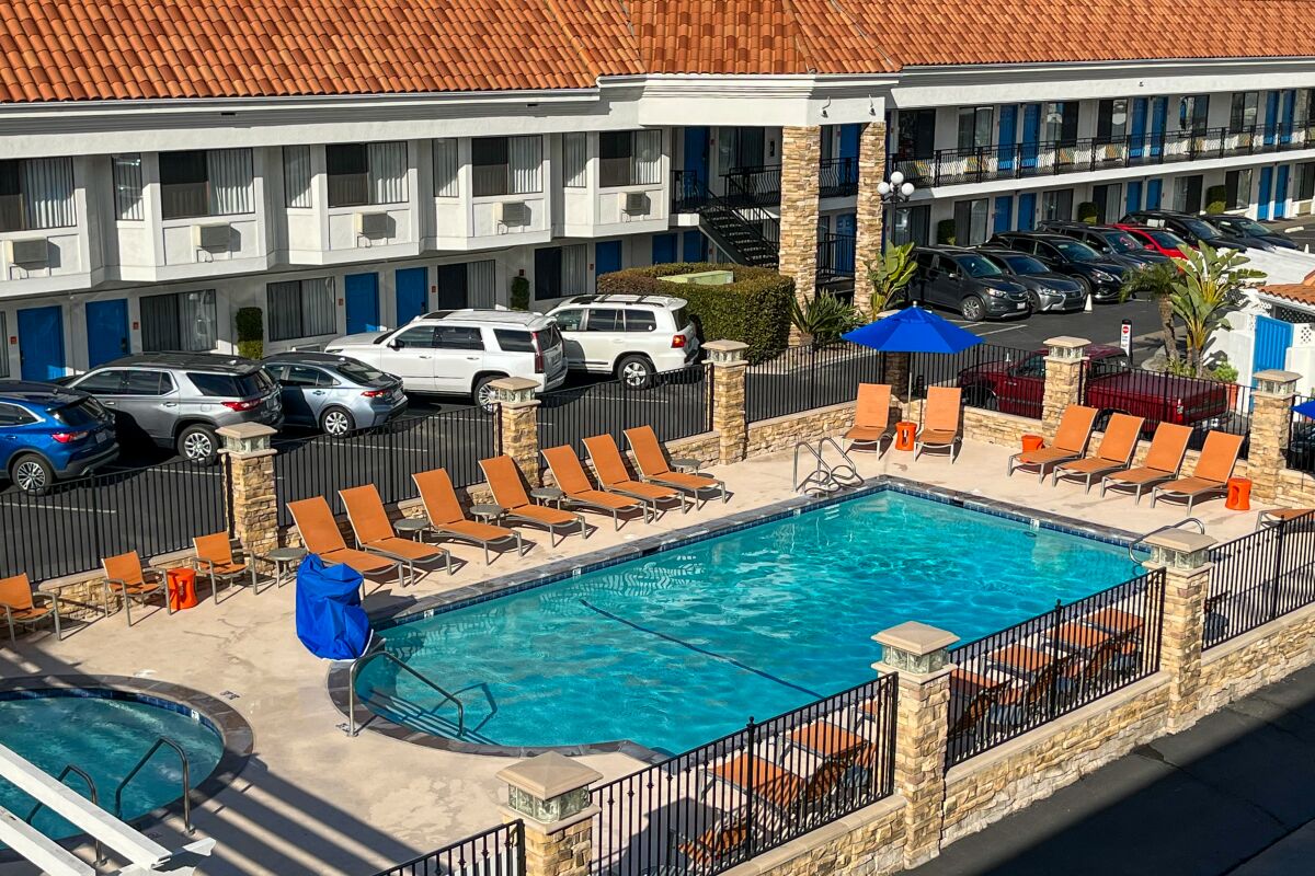 Loungers clustered around an outdoor pool next to a parking lot in front of a hotel