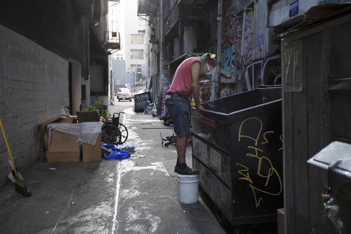 A man climbs into the garbage bin in an alley in Los Angeles.
