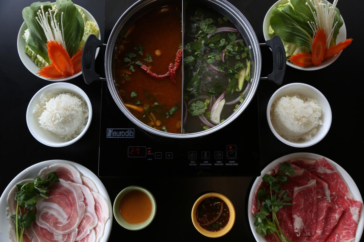 Two broths, the tom yum with pork belly, left, and Thai herb broth with prime beef at Suki Time in Lomita.