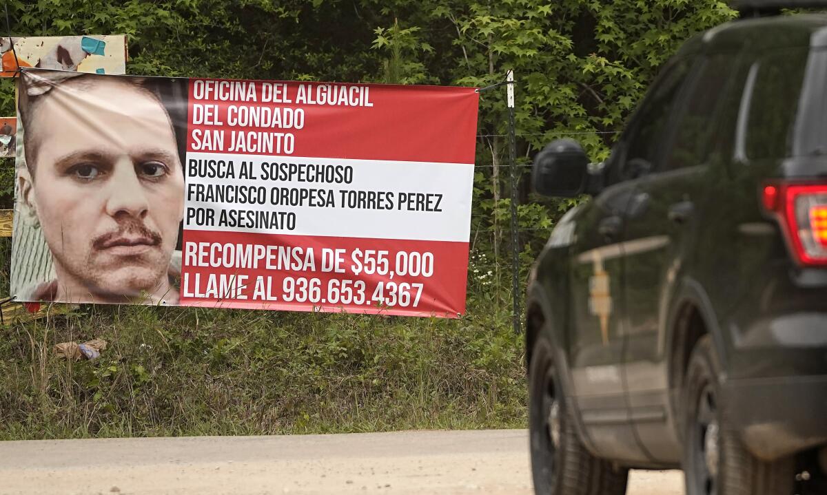 A black vehicle approaching a Spanish-language "Wanted" sign erected beside a road, featuring a large closeup of a man.
