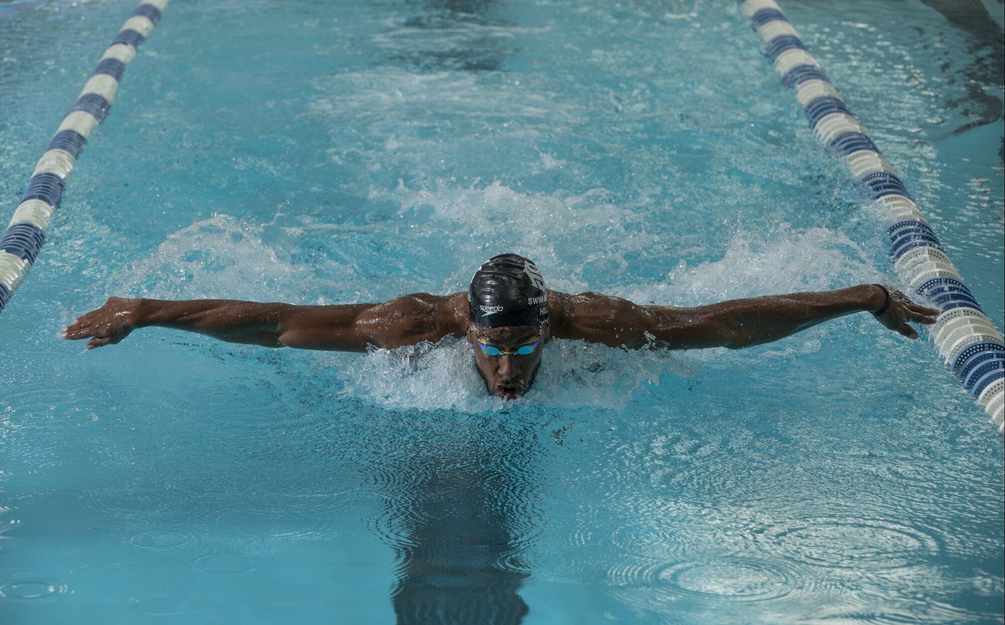 Jamal Hill lifts his head out of the water with his arms stretched out on both sides as he swims the butterfly stroke.
