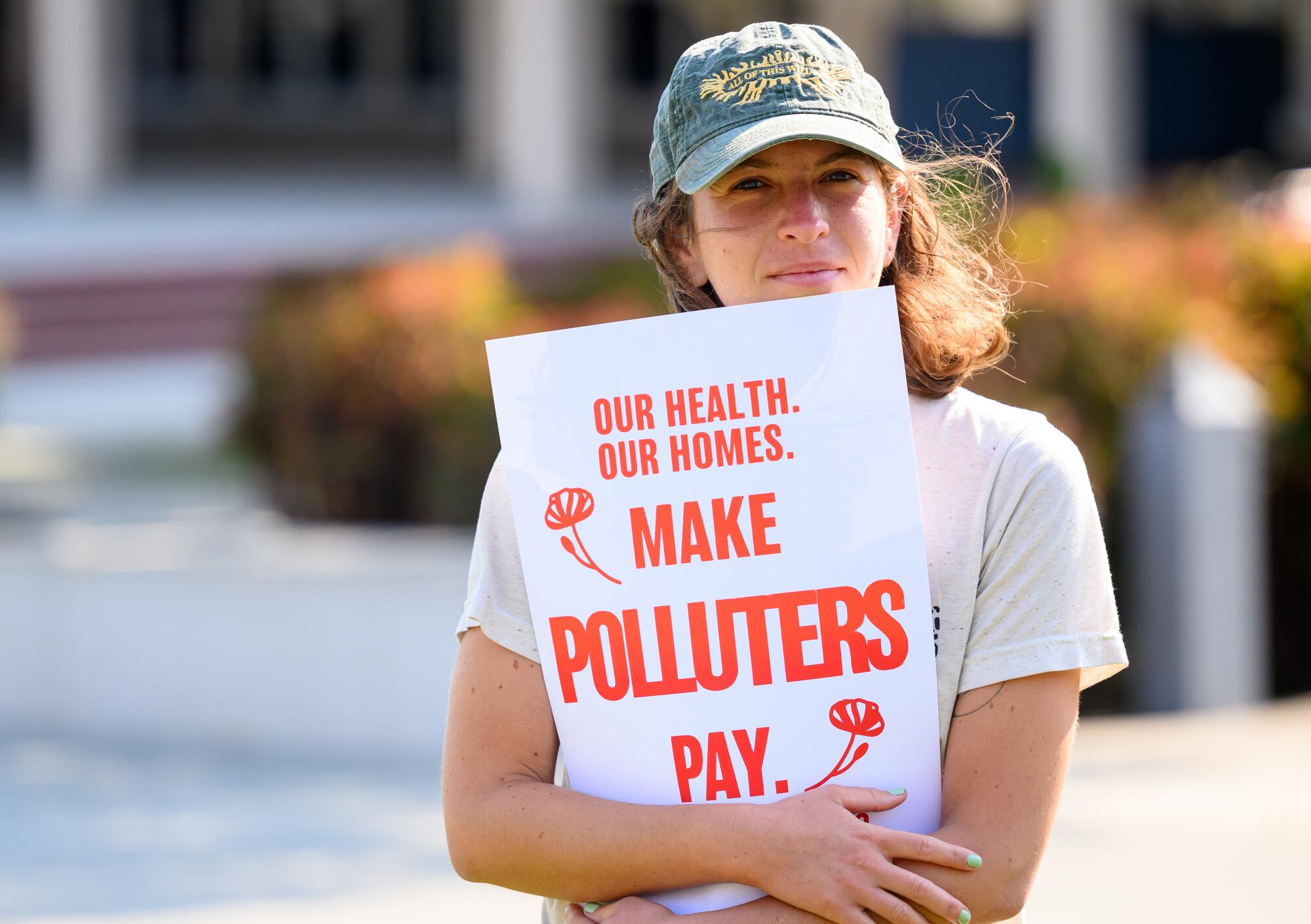 A woman in baseball cap holds a sign saying "Make Polluters Pay." 