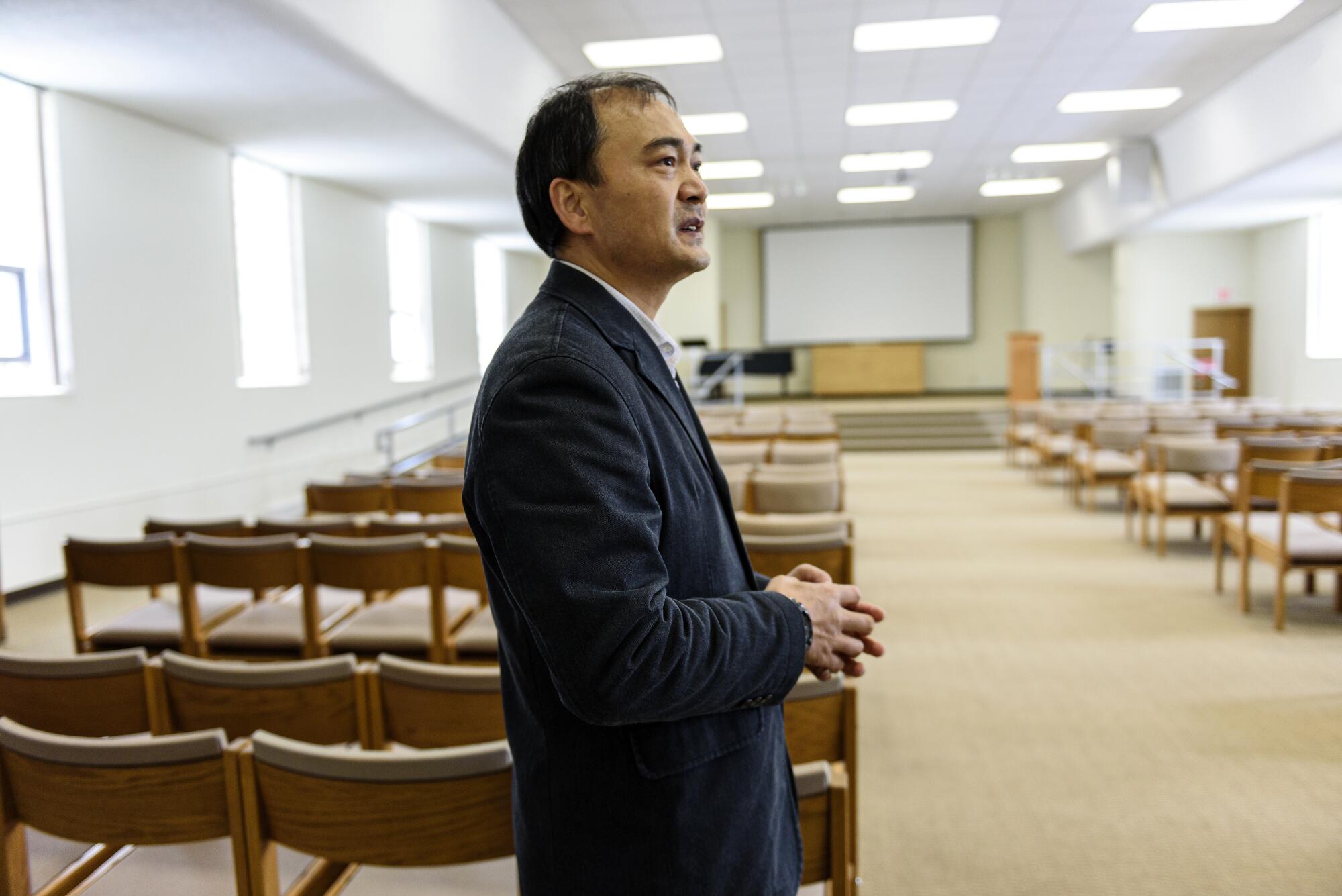 The Rev. Yuanlai Zhang stands in front of rows of chairs at his church