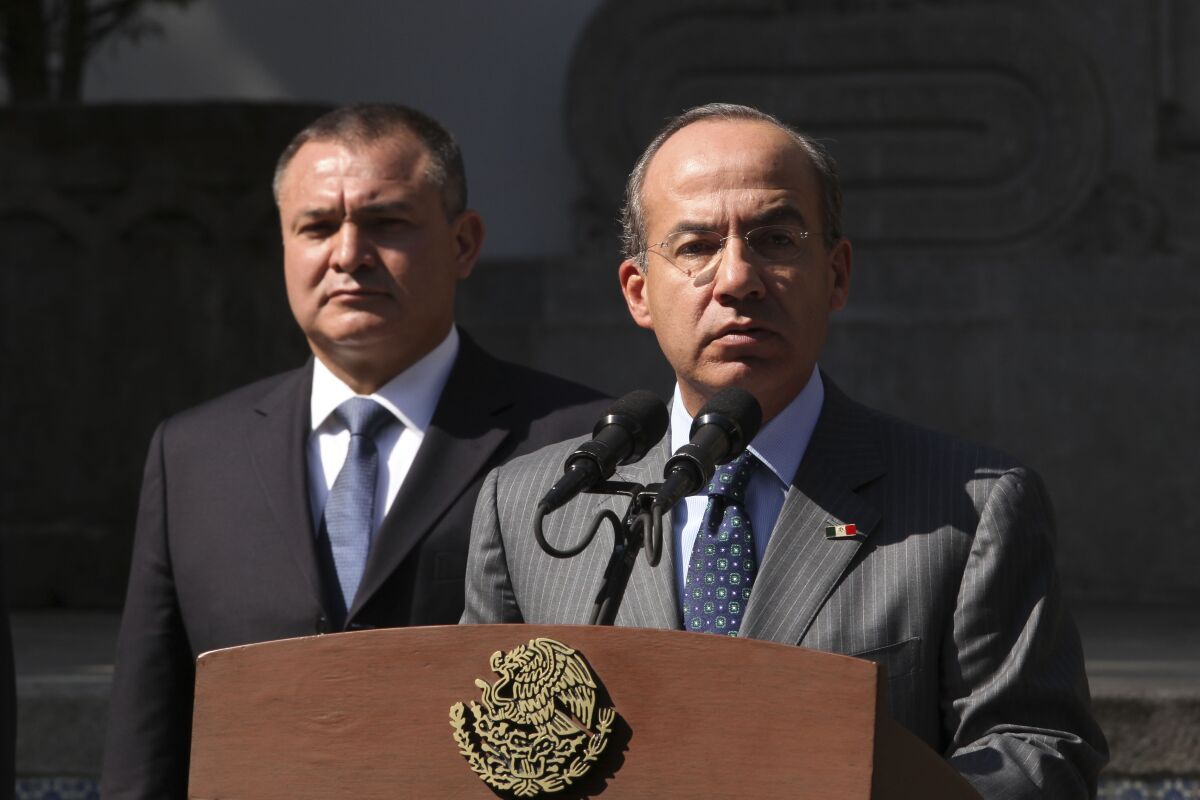رئیس جمهور مکزیک فیلیپه کالدرون در حالی که جنارو گارسیا لونا پشت سر او ایستاده است با میکروفون صحبت می کند.