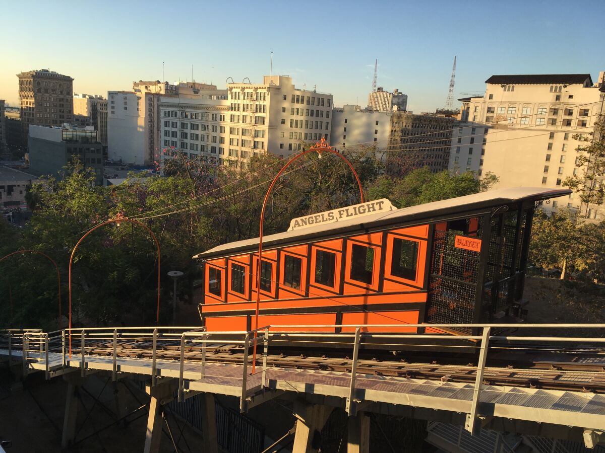 An orange cable car on a sloped track overlooking buildings in downtown Los Angeles.