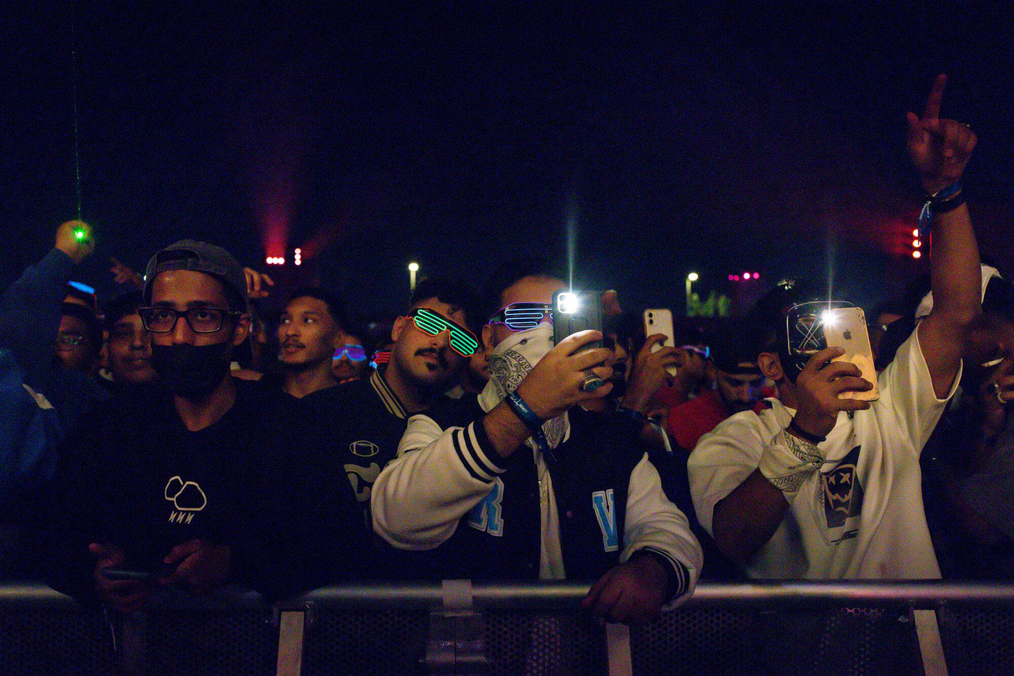 Concertgoers at a music festival hold up cellphones and wear glow in the dark glasses.