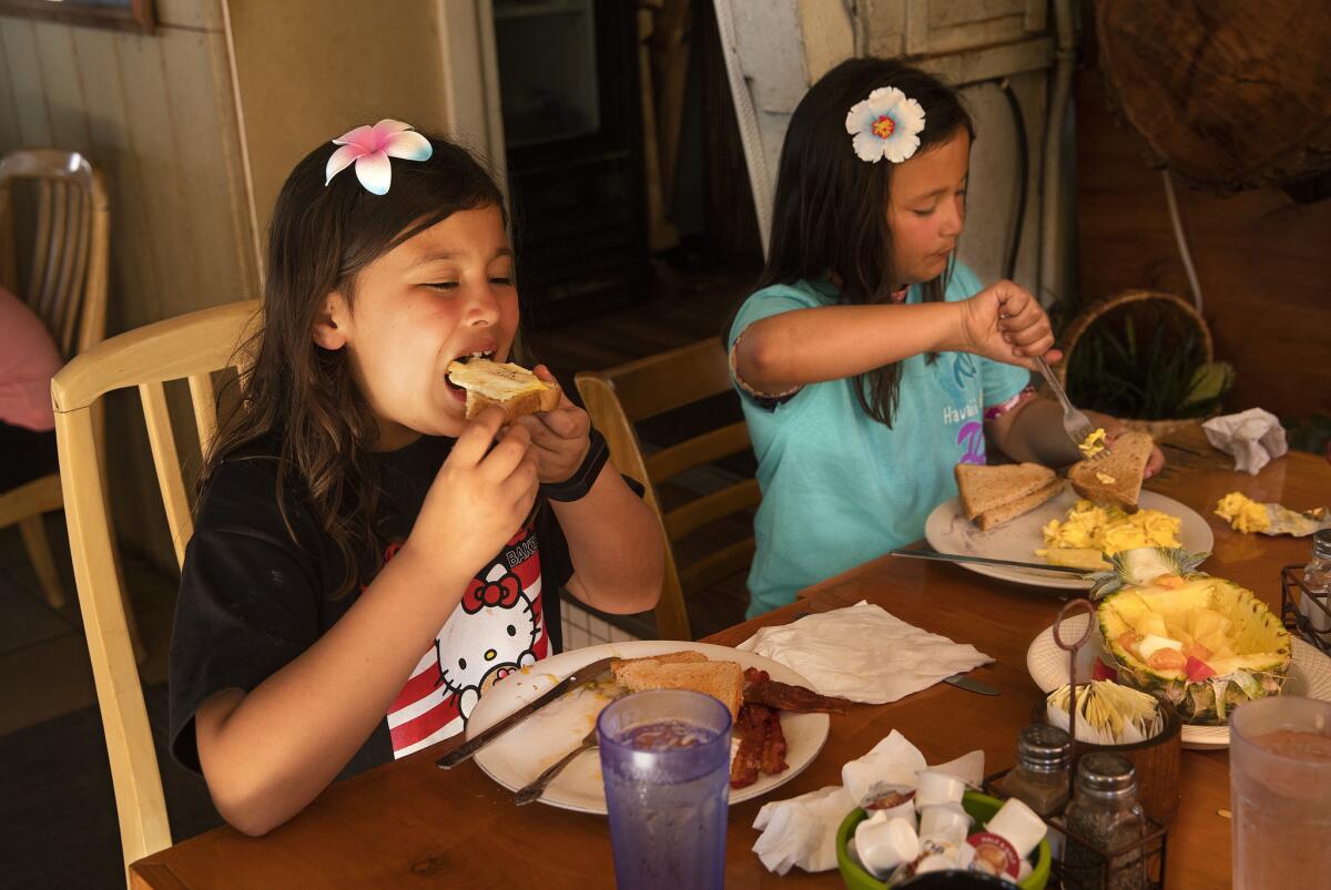Georgia Holland, 8, left, and her twin sister JoJo, enjoy breakfast at the Sunrise Cafe in Lahaina, Maui.