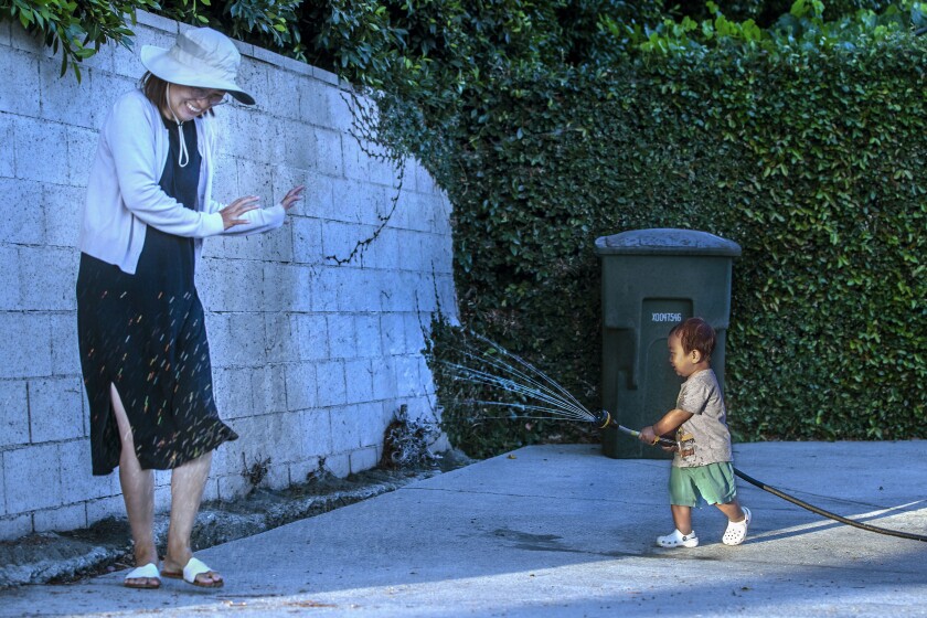 ARCADIA, CA - JUNE 10, 2021: Ian Choi, 21 months old, aims a hose at his mother Younkyung Ko, while playing in front of their home on Altura Rd. in Arcadia. Choi grabbed the hose from his father Tony Choi after he used it to wash his car. (Mel Melcon / Los Angeles Times)
